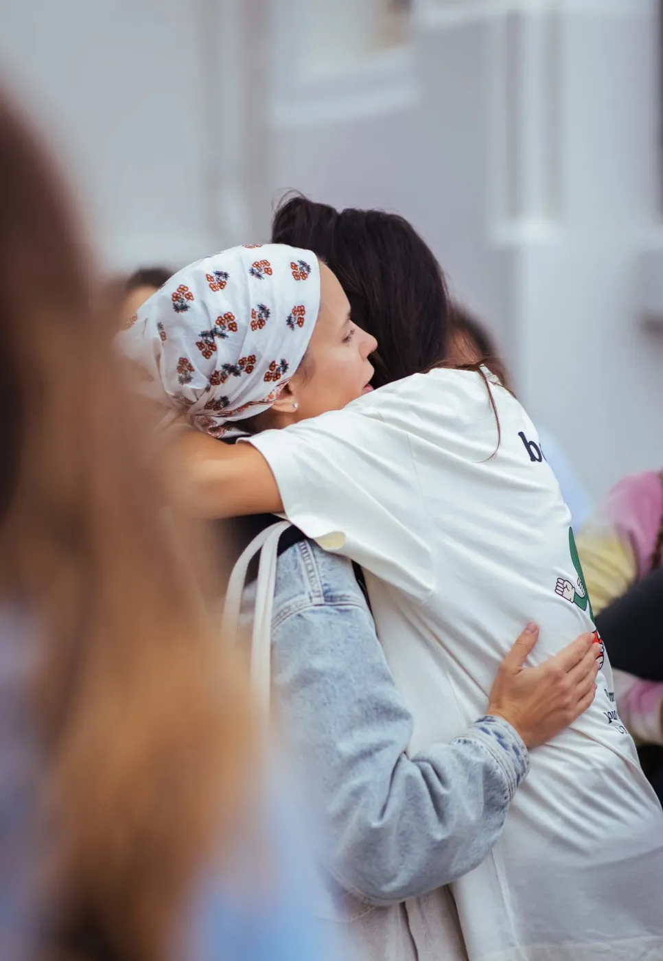 Deux femmes se serrent dans les bras lors d’un événement du club, l’une porte un foulard noué sur la tête