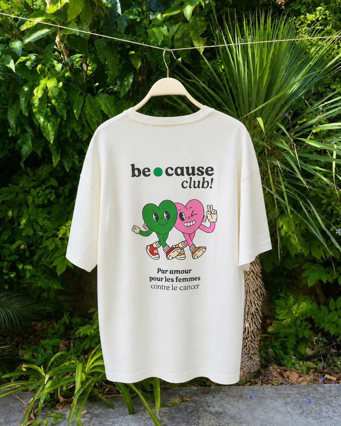 Le tee-shirt du club suspendu dans un jardin : logo be.cause club, les deux cœurs et la devise « Par amour pour les femmes contre le cancer »